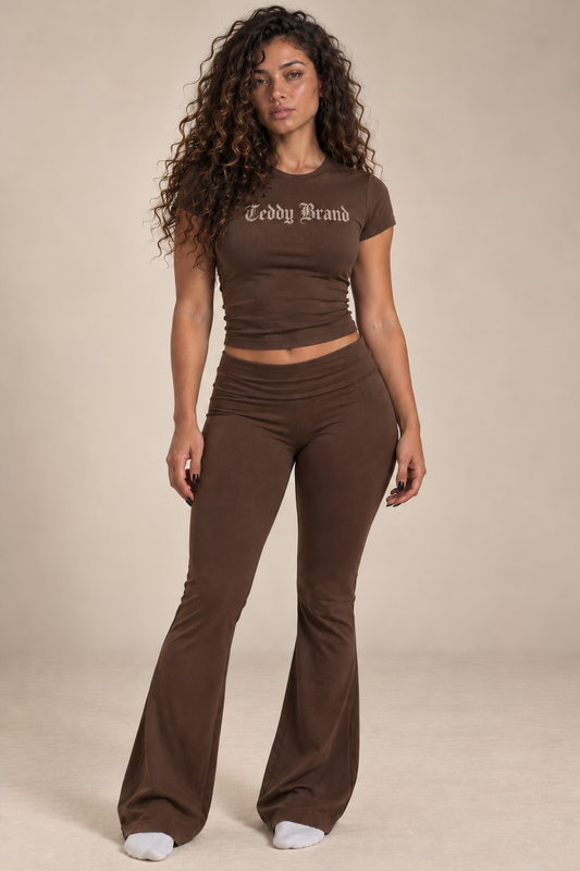 Front view of a model wearing the Mocha Brown Lounge Set with faded ivory Gothic Teddy Brand chest lettering, a fitted short-sleeve top, and fold-over flared pants.